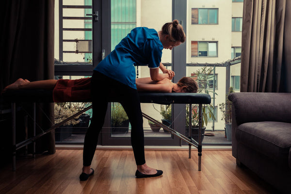 A massage therapist is treating a female client on a table in an apartment 