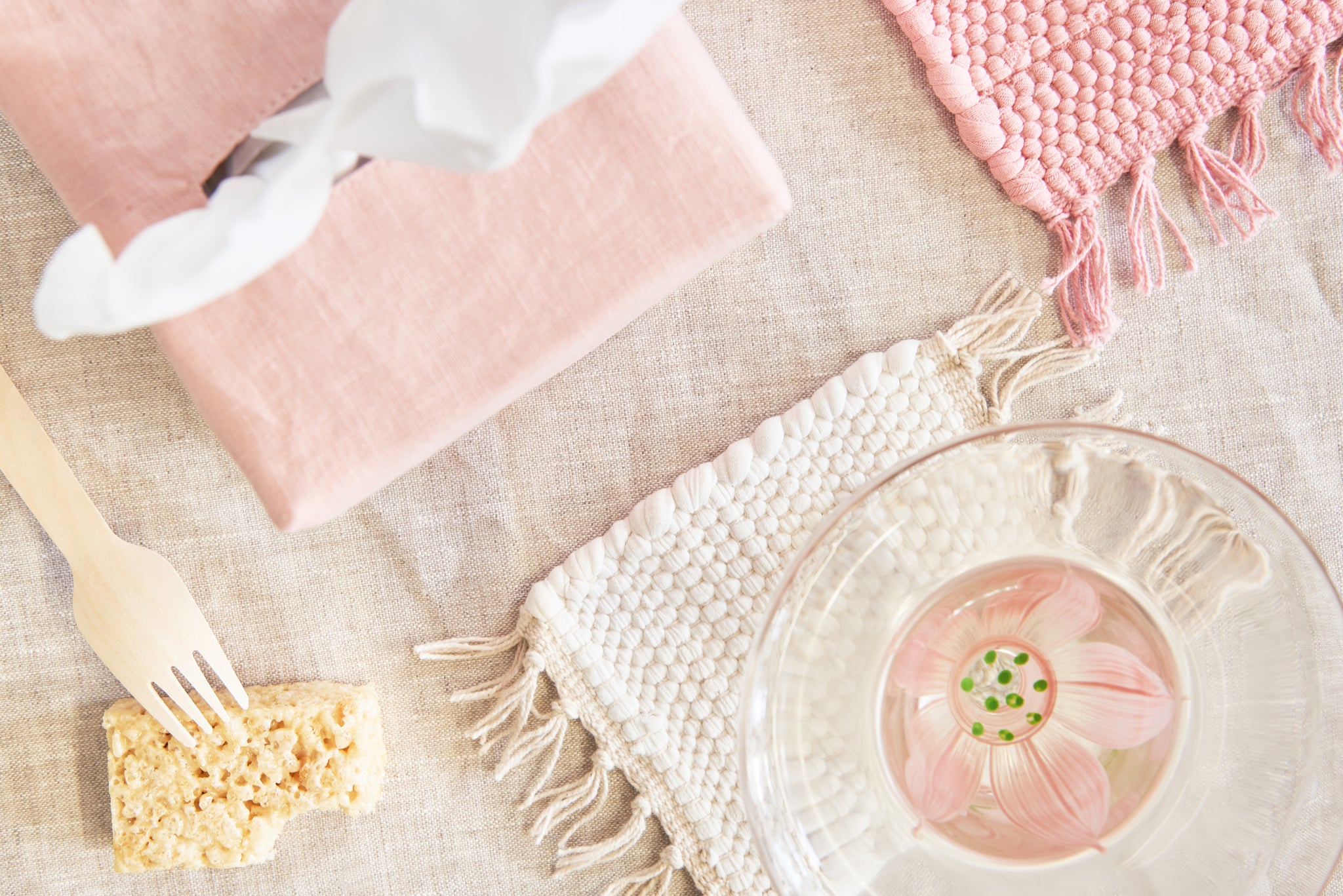 flat lay, tissue box with pink cover, rice krispie treat with wooden fork, cream rug coaster, pink rug trivet
