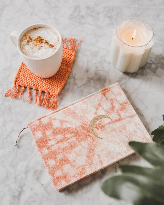 coffee mug on top of orange rug coaster, orange journal, white lit candle