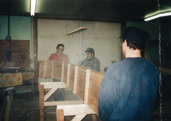 Three men in the workshop, lifting a wood toboggan onto its side