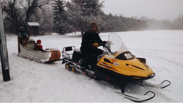 Young man, pulling his family in a traditional rigged toboggan behind his yellow snowmobile