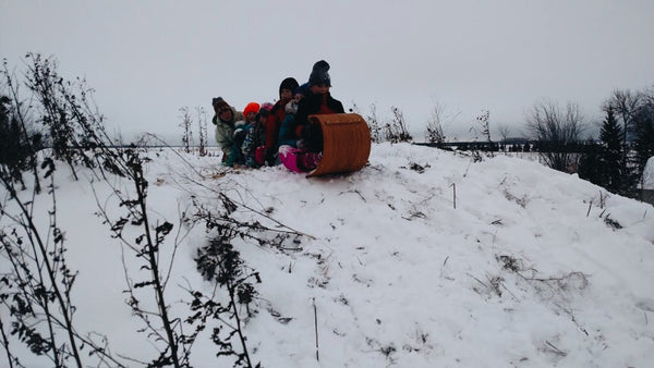 Four kids packed into a toboggan, siting atop a snow-covered hill