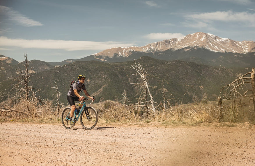 Cyclist on gravel road passing snow capped peaks