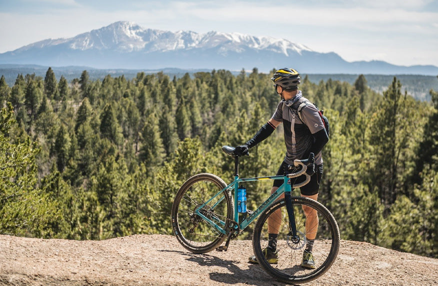 Cyclist with gravel bike looking over shoulder an snow-capped mountain range in Colorado