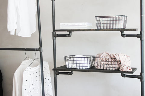 Shelves in dark pine being hold by a cloths rack made of black water pipes. Some simple and clean accessories and clothes are stored on it.