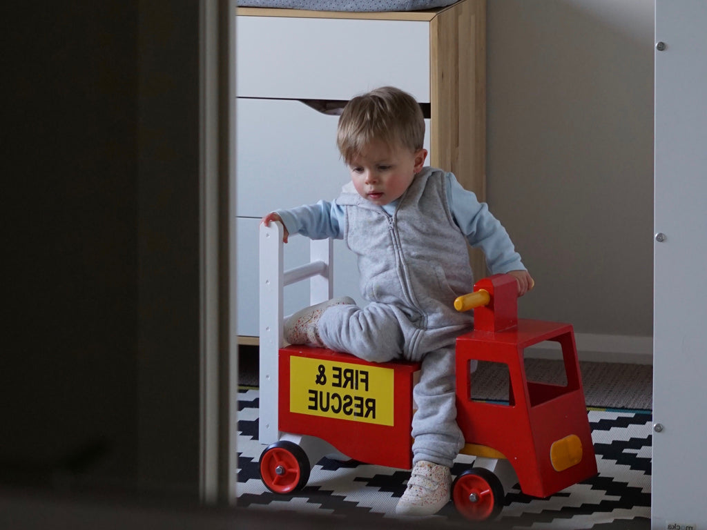 little boy on a toy firetruck in a bedroom