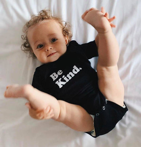 Baby wearing a one-piece shirt with the words Be Kind.