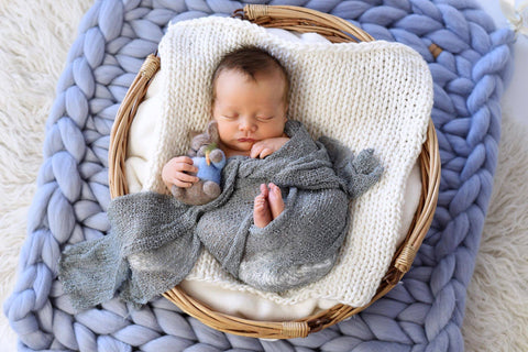 Newborn baby posed in a basket on top of a chunky knit blanket