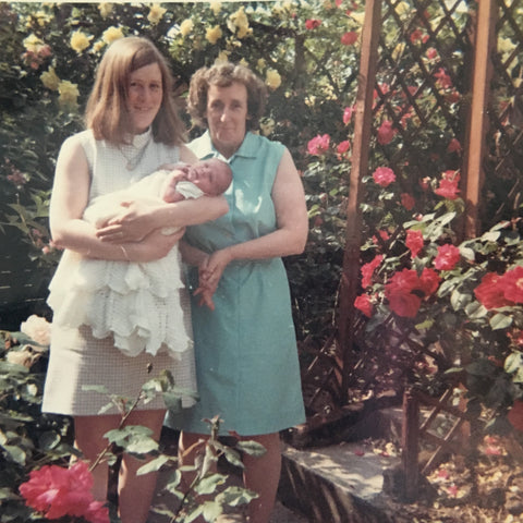 a young mother with her mother and a baby in a rose garden