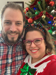 image of white brunette woman smiling enthusiastically with her husband dressed in red and green festive Christmas outfits.