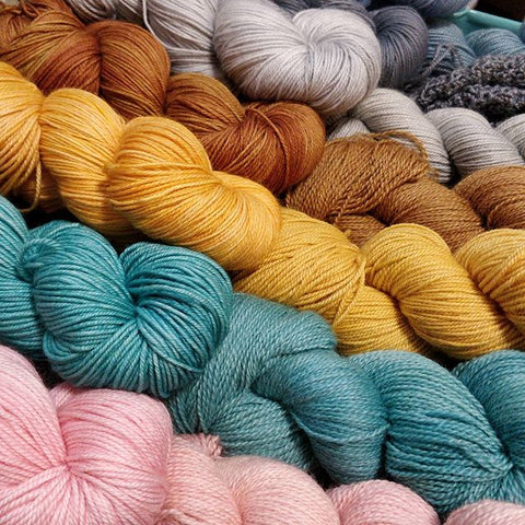 Skeins of yarn lay on a diagonal in colours pink, teal, yellow, copper, light grey, dark grey