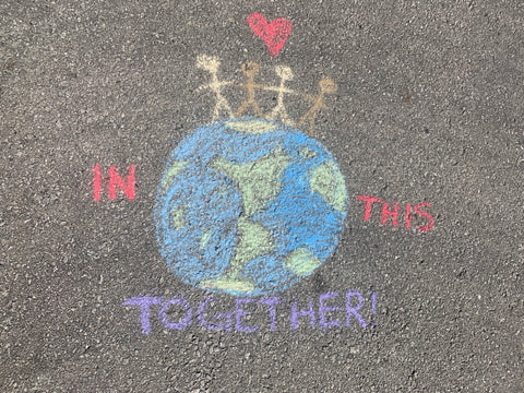 Chalk Drawing of the earth with people holding hands on top with the words "In this together"