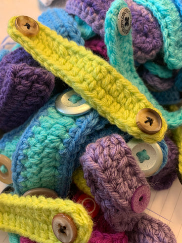 A pile of brightly coloured crocheted mask extenders with two buttons on each one.  