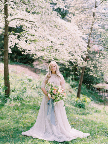 Bride under cherry blossoms holding bouquet with blue silk ribbon by The Lesser Bear Photography Jenny Haas Florals Passiflora Studios Design and Planning Auburn and Ivory Creative 