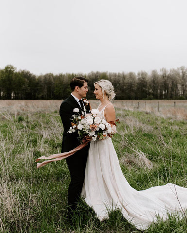 Married couple photographed in a field with bouquet and silk ribbon by The Lesser Bear