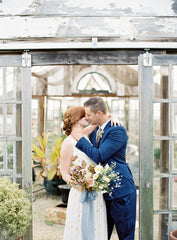 Bride and Groom kissing. Bride in floral printed dress groom in a navy suit with bridal bouquet and blue ribbon by The Lesser Bear. Photo Jenna Powers Florals Old Slate Farm