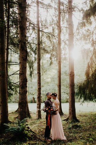 Bride and Groom in a grove of tall trees and moss. Photo by Addison Jones Florals by Bear Roots Floral and Custom Red Ribbon by The Lesser Bear