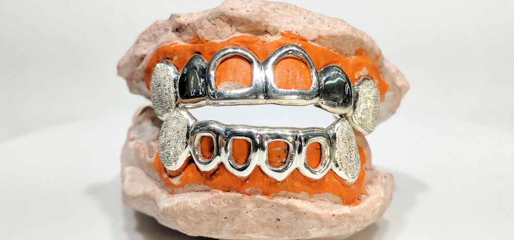 In the center: a custom made sterling silver top and bottom grills with open face and laser cut canines made by Popular Jewelry in New York City for Rujhen
