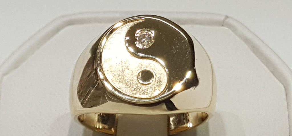 In the center: a custom made signet ring with a Yin Yang design on top in 14 karat yellow gold high polish and diamond made by Popular Jewelry in New York City