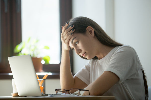 Woman with her hand on her forehead, looking stressed and staring at her laptop screen