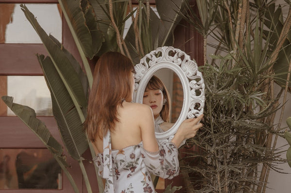 Asian young woman looking at a mirror. Pink room with plants on the background.