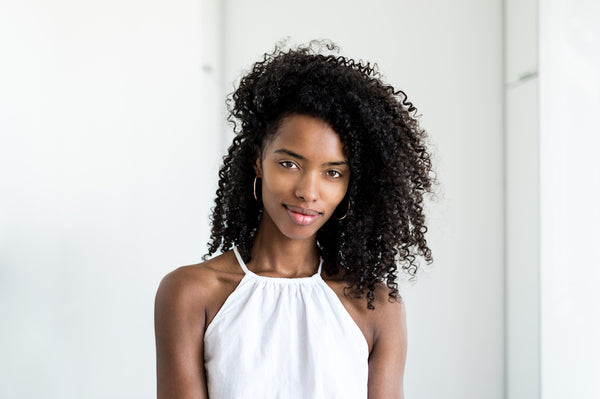 Dark skin woman with long curly hair and white blouse.