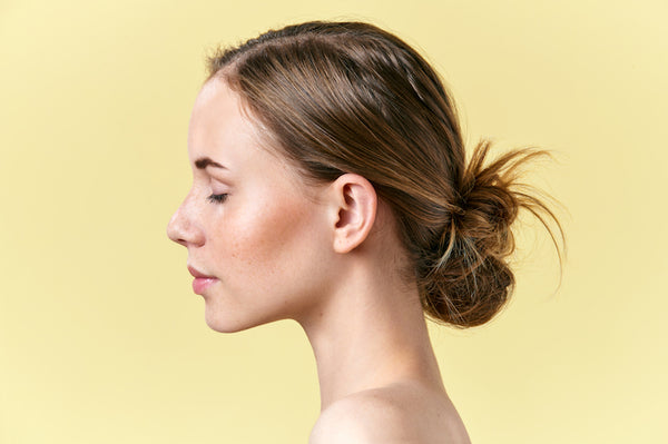 Redhead woman with freckles, with light nude make-up, closed eyes, isolated on pastel yellow background portrait