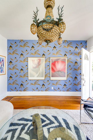 Inside a home with an eclectic chandelier and  vivd blue wallpaper with a pattern in gold