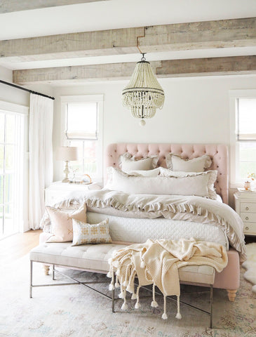 A beautiful bedroom with a chandelier and pink tufted headboard