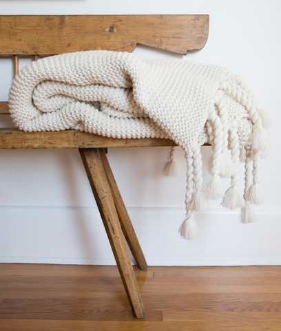 a folded white knit throw on a bench