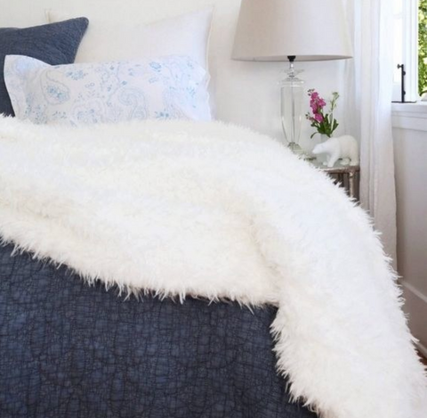 A fluffy white throw blanket on a blue bed