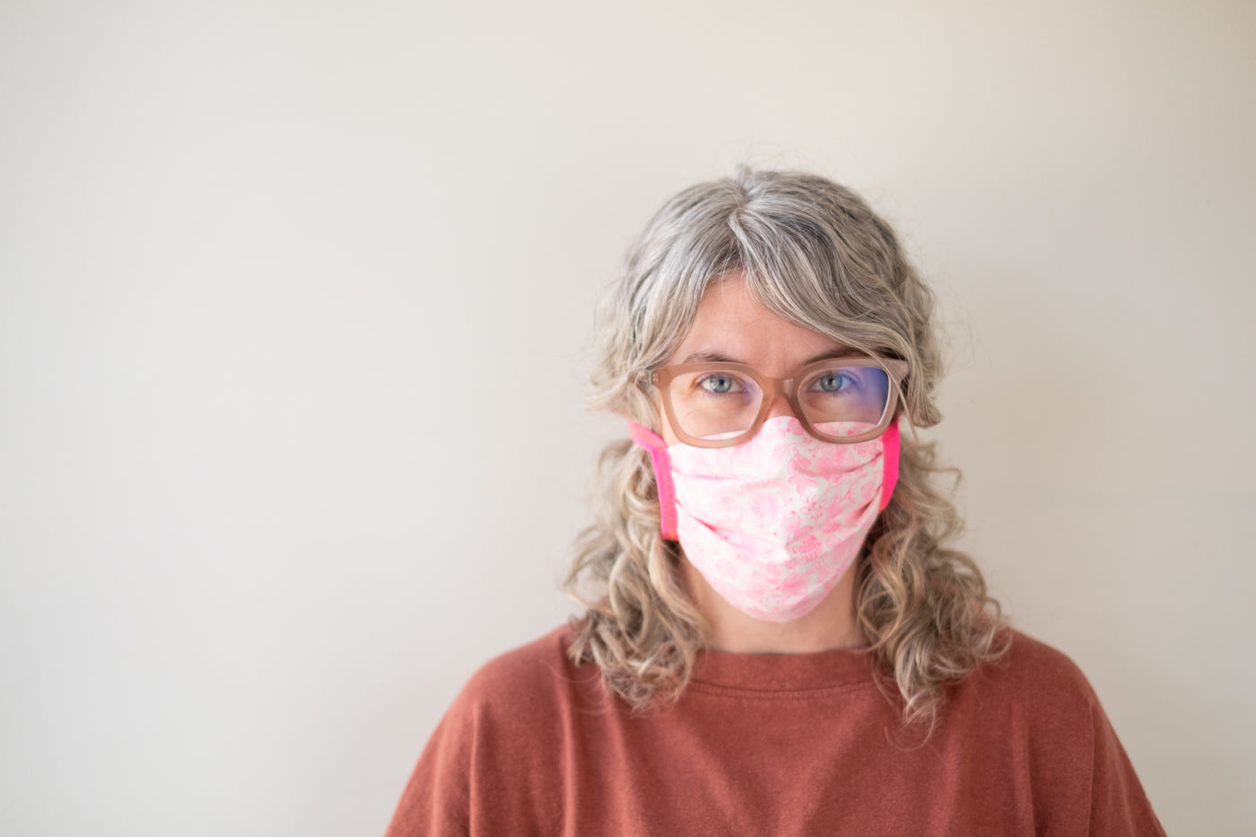 Jaime wearing a pink face mask with bright pink ties standing in front of a white wall.