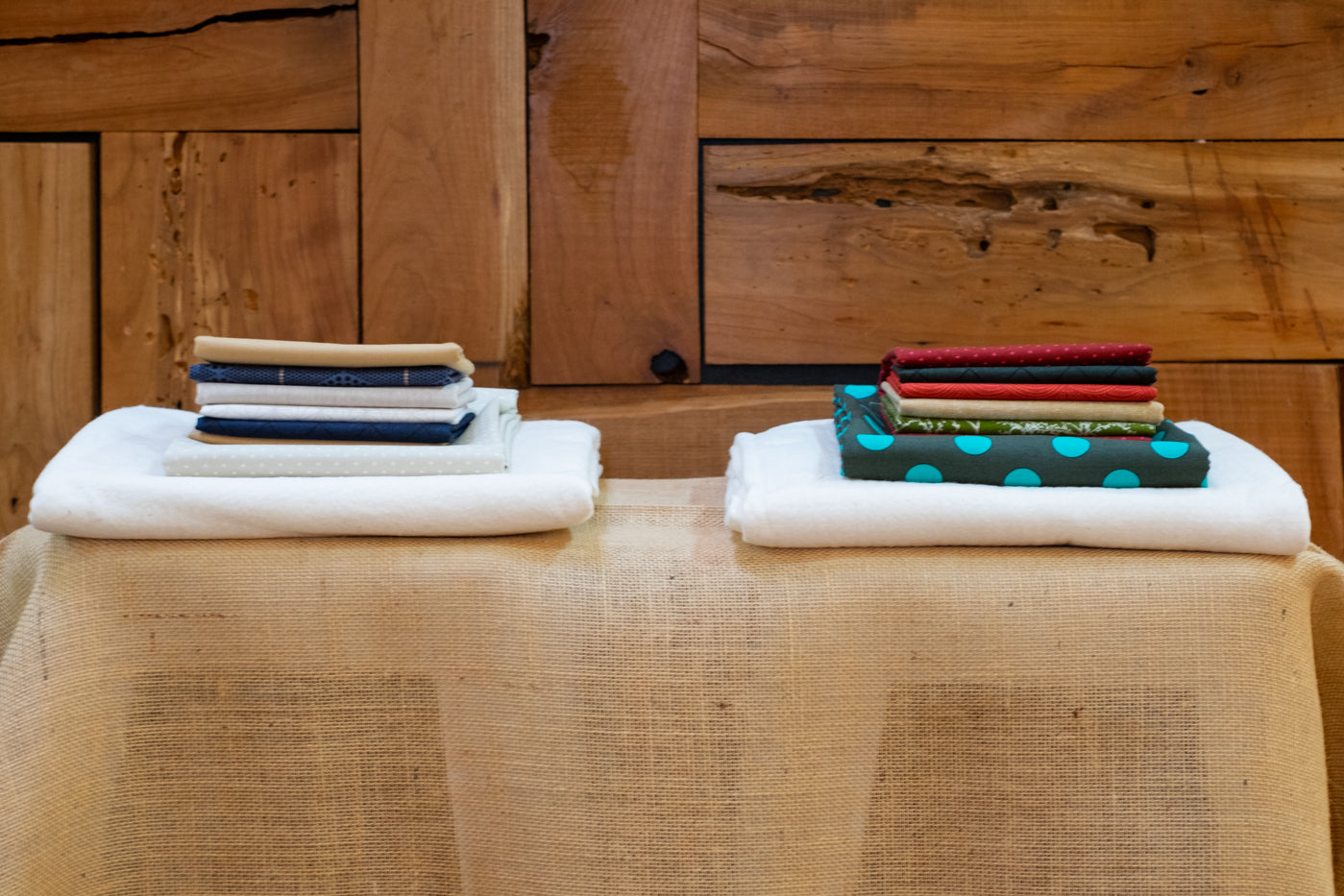 Material perfectly folded in two separate piles, on top of a burlap table with wooden backdrop.