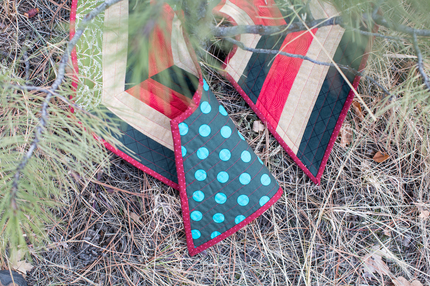 Photograph taken of a pine tree outside looking straight down at a tree skirt that is flipped open on one end to show the decorative backside of the tree skirt.