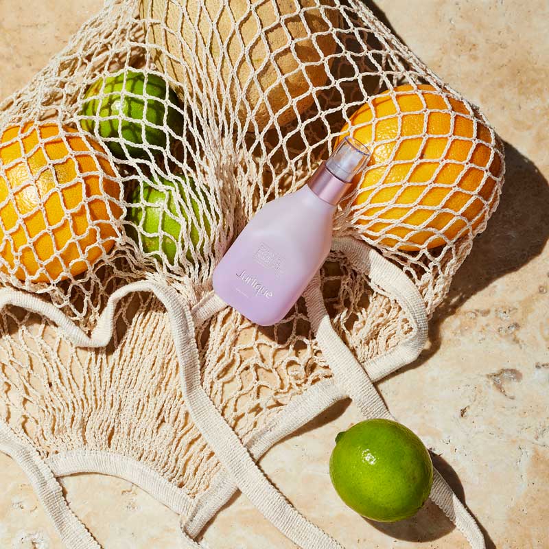 Jurlique Lavender Hydrating Mist placed on top of a netted shopping bag filled with lemon, limes and oranges.