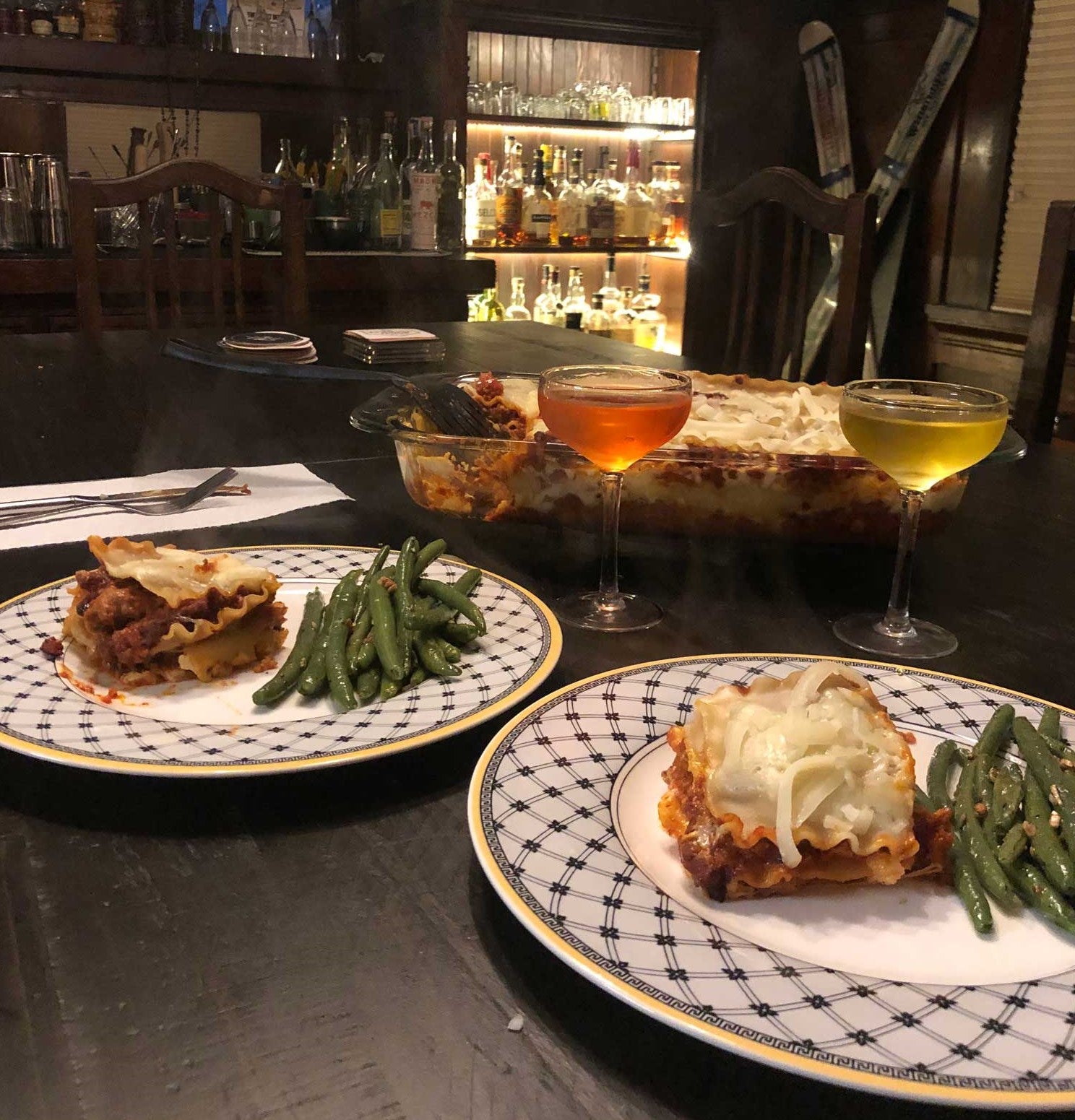 Plate of lasagna and green beans, in front of coupe glasses