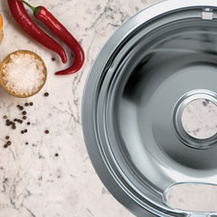 Image shows a portion of a shiny chrome drip bowl on a countertop, with chili peppers and seasoning in the background.