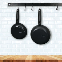 Wooden countertop with white backslpash features black hanging pot rack bar on backsplash. Two skillets hang from the bar.