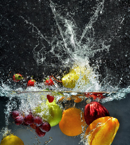 Various fruits and vegatables sit beneath water, some splashes of water are visible.