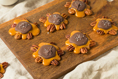 Pecan candies made of caramel, chocolate and pecans shaped like turtles on a wooden cutting board.