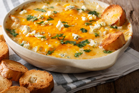 Buffalo chicken dip in a white bowl with accents of cheese and green onions. SMall pieces of toasted bread sit off to the side. 