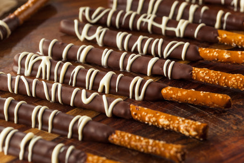 Dark chocolate dipped pretzel rods with drizzled white chocolate sit on a table, drying.