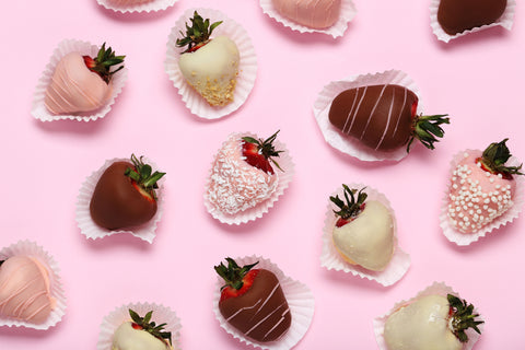 Pink background with images of white chocolate and dark chocolate dipped, decorated strawberries on individual papers.