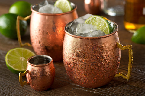 Copper mugs featuring liquid and a lime wedge on the rim of the mug on a counter background.