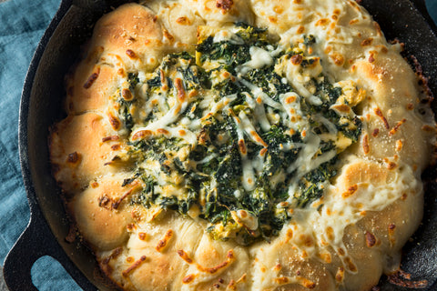 A cast iron pan holds a bread bowl full of creamy, green dip.