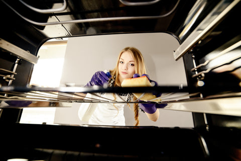 An image taken inside of an oven shows a woman facing the oven, holding a sponge to clean it.