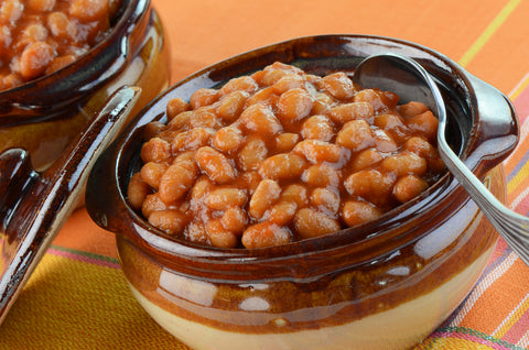 A vintage pottery pot with lid filled with baked beans sit on a table.