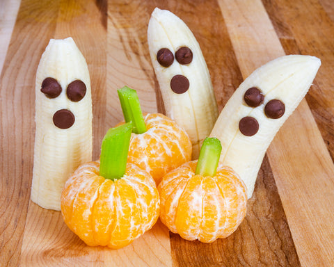 Mandarin oranges toped with small pieces of celery, and cut, peeled bananas with chocolate chip eyes and mouth on a wooden background.