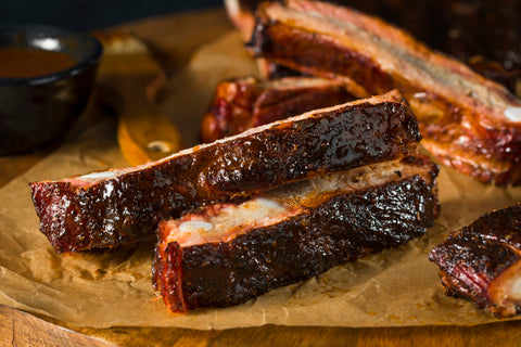 Juicy, individual smoked ribs sit on a wooden cutting board.