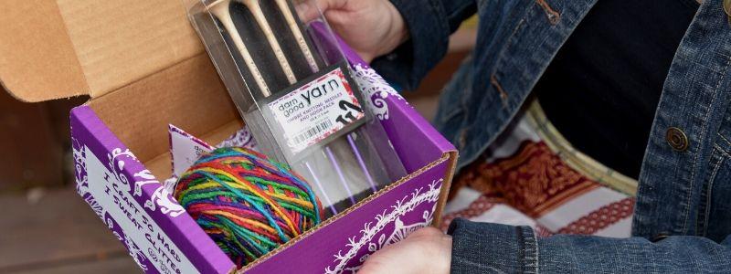 Hands holding a purple box with yarn and knitting needles inside